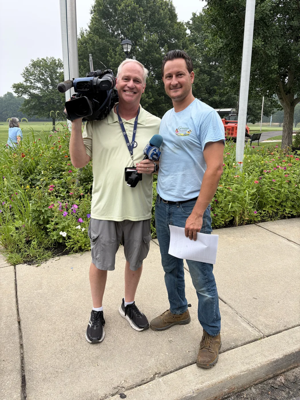 A news cameraman with a volunteer at the edge of the park, there to cover the volunteer day